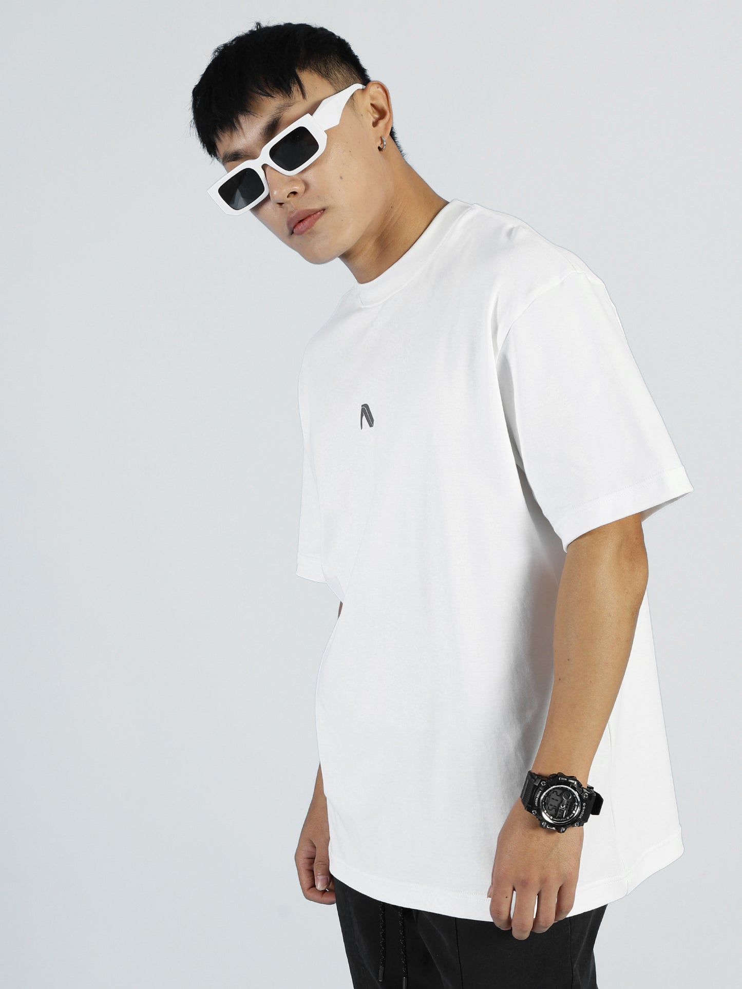 A modern trailblazer in My Store’s Vibe T—Bright White for Men pairs white sunglasses, a black wristwatch, and black pants against a plain light background, exuding athleisure style in this premium cotton-blend tee.